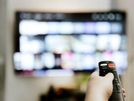 Hand holding remote control pointing to TV. Person watching smart television